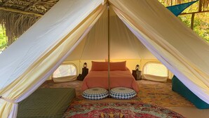 A tent with a bed, two pillows, a lantern, and a patterned rug.