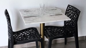 Een eettafel met een marmeren blad en een gouden onderstel, omringd door twee zwarte stoelen met een rasterpatroon.