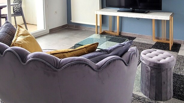 Een woonkamer met een bank, een bijzettafeltje, een televisie op een standaard en een schuifdeur die leidt naar een balkon.