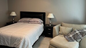 Un dormitorio con una cama, dos mesitas de noche con lámparas, un ventilador de techo y un sofá.