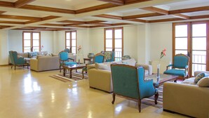 Un salón amplio con vigas de madera en el techo, ventanas grandes y varias zonas de estar, incluyendo sofás y sillones.