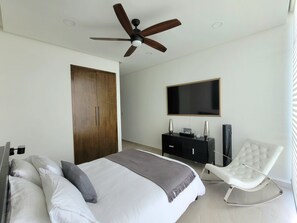 A bedroom with a bed, a TV, a wardrobe, a chair, and a ceiling fan. - Luxury Beachfront Condo in Rosarito with Pool & Jacuzzi (Playas de Rosarito)