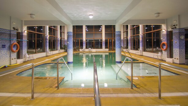 An indoor swimming pool with clear glass walls, metal railings, and a tiled floor. - Hotel y Cabañas Llanuras de Diana- Caja Los Andes (Natales)