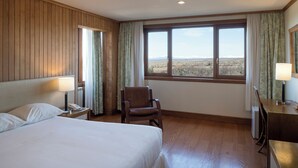 A hotel room with a bed, a chair, a desk, and a large window offering a view of the landscape. - Hotel y Cabañas Llanuras de Diana- Caja Los Andes (Natales)