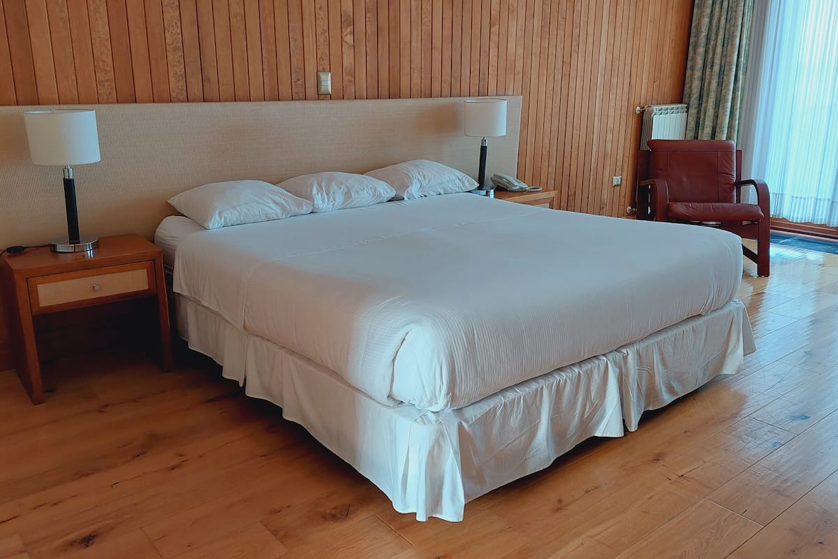 Ein großes Bett mit weißer Bettwäsche, zwei Nachttische mit Lampen, ein Holzboden und ein Holz-Kopfstück.