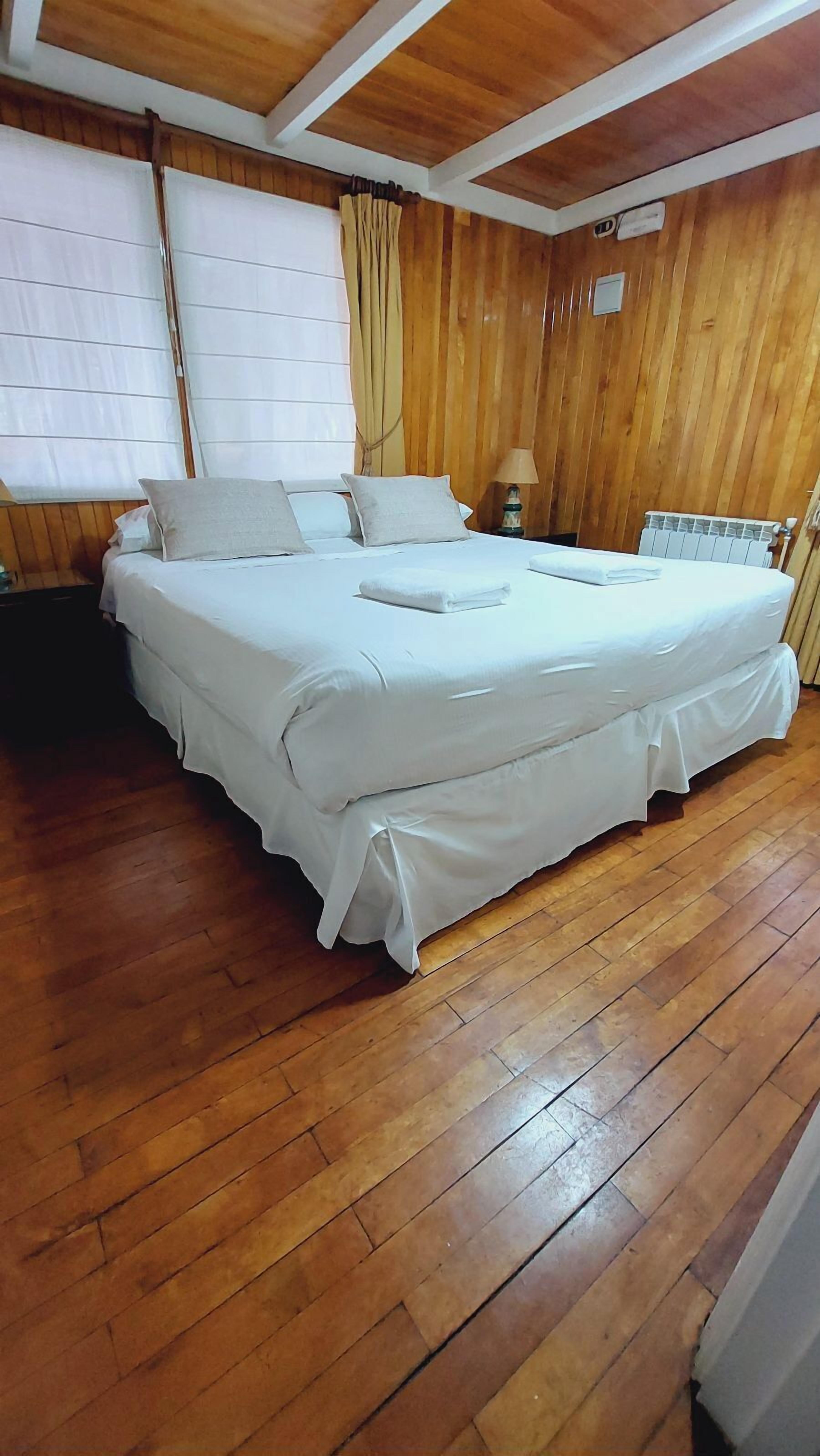 A large bed with white bedding in a room with wooden walls and floors.
