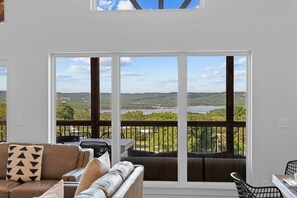 Ein Balkon mit Blick auf einen See und Hügel, ausgestattet mit einer Couch und Sesseln.