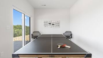 A ping pong table with two chairs, a table tennis paddle, and two wall-mounted abstract art pieces.