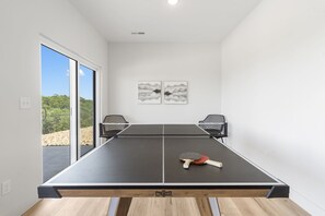 Une table de ping-pong avec deux chaises, une raquette de tennis de table et deux œuvres d’art abstraites fixées au mur.