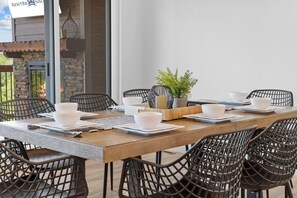 A dining area with a long wooden table, black wire mesh chairs, white bowls, and a potted plant.