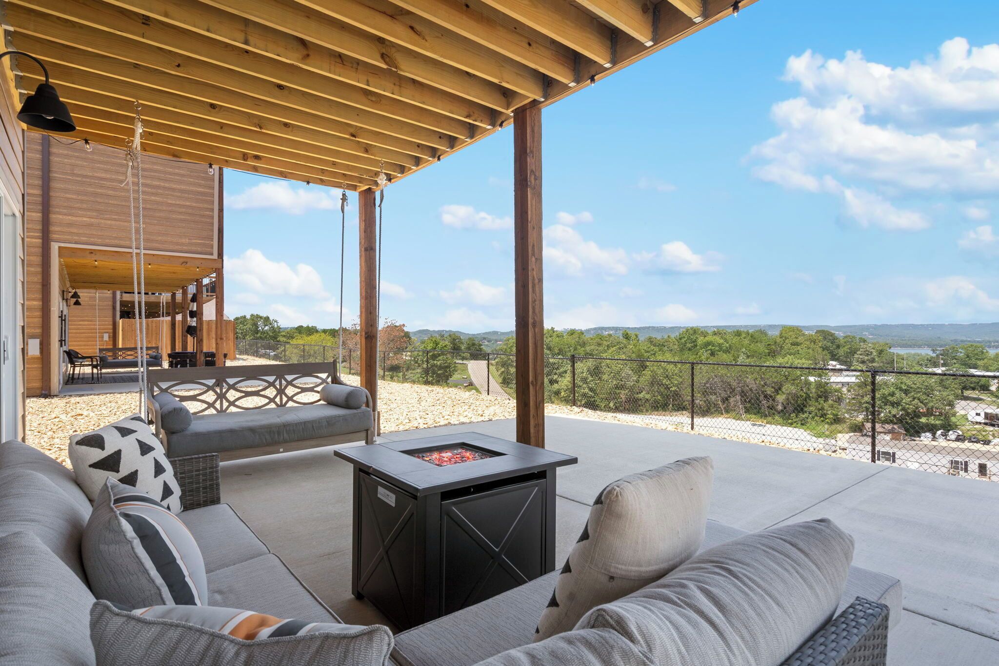Une terrasse extérieure dotée d’une pergola en bois, d’un foyer intégré dans une table et d’un canapé avec des coussins.