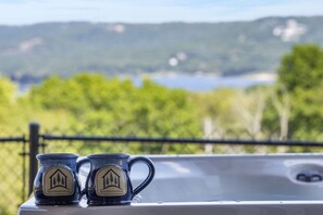 Deux tasses ornées du logo d’une entreprise sont posées sur une table près d’une fenêtre donnant sur un lac et la verdure environnante.