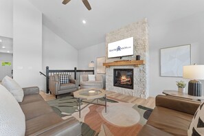 A modern living room with a fireplace, a mounted television, and a staircase leading to another level.