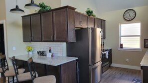 A modern kitchen with dark wood cabinets, a stainless steel refrigerator, a bar area with bar stools, and a window with blinds. - Ozarks View with Cornhole, Pickleball, Community Pools, Firepit,  Free Tickets and More (Kimberling City)