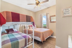 Ein Schlafzimmer mit Etagenbetten, Deckenventilator, Fenster mit Vorhängen und einem gerahmten Zitat an der Wand.