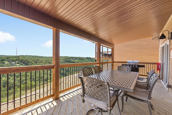 Eine überdachte Terrasse im Freien mit Holzboden, einem Metalltisch und -stühlen und Blick auf eine grüne Landschaft.