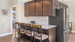 A kitchen with dark wooden cabinets, a stainless steel refrigerator, and a bar area with four chairs. - Ozarks View with Cornhole, Pickleball, Community Pools, Firepit,  Free Tickets and More (Kimberling City)