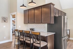 A modern kitchen with dark wooden cabinets, a stainless steel refrigerator, and a bar area with four chairs.