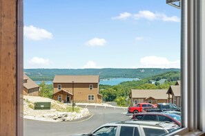 A view of a parking lot with several cars, a building with a wooden facade, and a scenic backdrop of hills and a body of water. - Ozarks View with Cornhole, Pickleball, Community Pools, Firepit,  Free Tickets and More (Kimberling City)