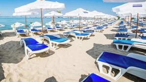 Una spiaggia con file di lettini bianchi e ombrelloni, un cielo blu limpido e l'oceano sullo sfondo.