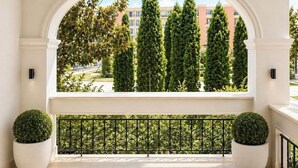 Un balcone con ringhiera bianca, piante in vaso e vista su alberi alti e palazzi.