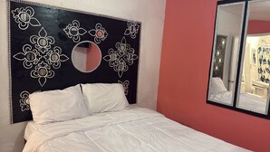 Een slaapkamer met een bed, een grote spiegel en een decoratief hoofdbord met bloemmotieven.