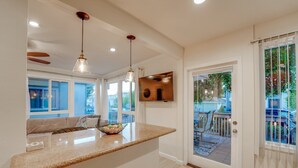 A kitchen with a granite countertop, pendant lights, and a view of the backyard through a glass door. - WindnSea Beach Perfection - Walk to Beach, Pet Friendly & Parking! (La Jolla)