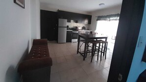 A compact kitchen with a refrigerator, stove, and sink. There is a dining area with a table and chairs. - Departamentos Velasco 2 (Tijuana)