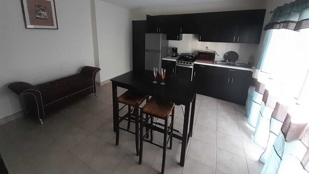 A compact kitchen with dark cabinets, a dining table with two chairs, and a bench in the corner. - Departamentos Velasco 2 (Tijuana)