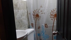 A small bathroom with a toilet, sink, and shower curtain with floral patterns. - Departamentos Velasco 2 (Tijuana)
