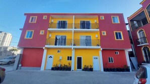A multi-story building with a red and yellow facade, balconies, and a gated entrance. - Departamentos Velasco 2 (Tijuana)