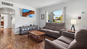 A modern living room with a wooden floor, a sofa, a coffee table, and a TV mounted on the wall. - Palmera Place Uptown Phoenix (Phoenix)