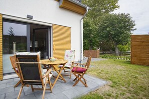 A patio with a round wooden table and chairs, a small easel, and a bowl of fruit.
