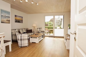 A cozy living room with a plaid sofa, a wooden coffee table, and a lamp. There is a sliding glass door leading to a balcony with outdoor furniture. - Ferienhaus Liva - Das Ferienhaus Liva in Dranske auf Rügen (Dranske)
