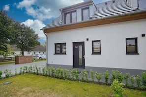 A single-story building with a black door, two windows, and a small garden area with young plants.