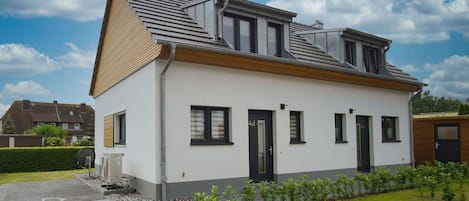 A modern two-story house with a sloped roof, a small front garden, and a paved driveway.