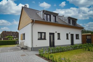 Una casa moderna su due piani, con tetto a falde, un piccolo giardino antistante e vialetto lastricato.