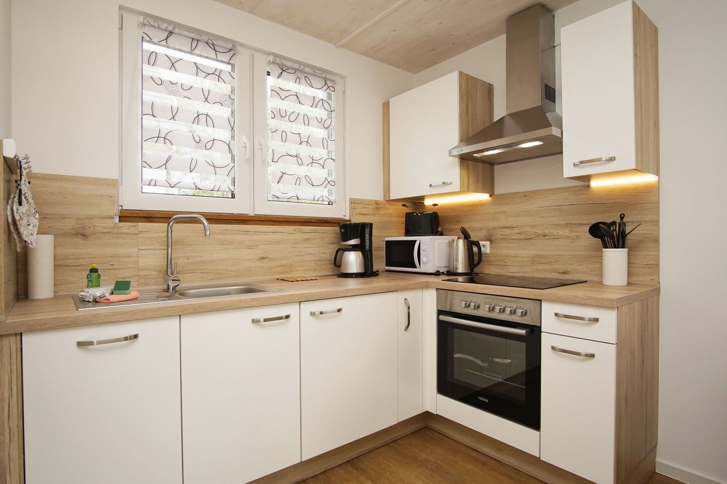 Una cucina moderna con mobili bianchi, forno in acciaio inossidabile, microonde e macchina per il caffè.