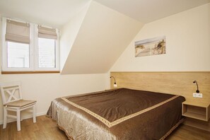 A bedroom with a bed, a chair, a nightstand, a painting, and a window with blinds.