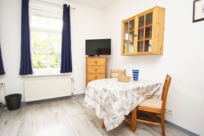 A room with a wooden table, a television on a dresser, a cabinet, and a window with curtains.