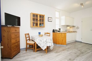 Eine kompakte Küche mit Essbereich, Holzschränken, einem Fernseher und einer kleinen Kücheninsel mit Kaffeemaschine.