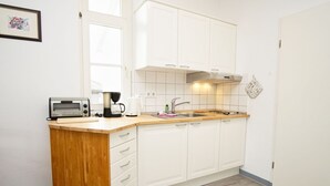 Eine kleine Küche mit weißen Schränken, einer Holz Arbeitsplatte, einer Kaffeemaschine und einem Toaster.
