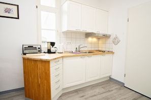 Eine kleine Küche mit weißen Schränken, einer Holz Arbeitsplatte, einer Kaffeemaschine und einem Toaster.