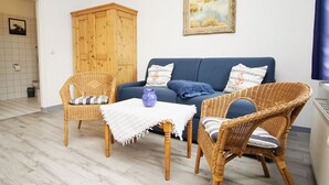 Ein gemütliches Wohnzimmer mit einem blauen Sofa, Korbstühlen, einem Holzschrank und einem gerahmten Gemälde an der Wand.