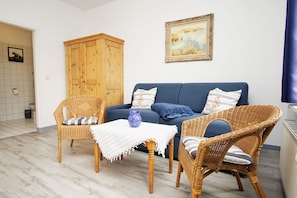 Ein gemütliches Wohnzimmer mit einem blauen Sofa, Korbstühlen, einem Holzschrank und einem gerahmten Gemälde an der Wand.