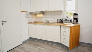 Una cucina compatta con mobili bianchi, un piano di lavoro in legno, un bollitore, un tostapane e una macchina da caffè.