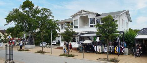Een wit gebouw met een balkon, een kraampje met kleding en een fiets ervoor.