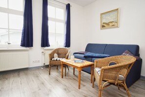 A room with a blue sofa, wicker chairs, a wooden table, and a window with curtains. - Die Ferienwohnung Nr. 02 im Haus Rugier in Göhren - Haus Rugier (Göhren)
