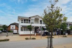 A two-story building with a white facade and a shop on the ground floor. - Die Ferienwohnung Nr. 02 im Haus Rugier in Göhren - Haus Rugier (Göhren)
