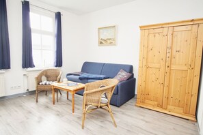 A room with a blue sofa, wicker chairs, a wooden table, a wardrobe, and a painting on the wall. - Die Ferienwohnung Nr. 02 im Haus Rugier in Göhren - Haus Rugier (Göhren)